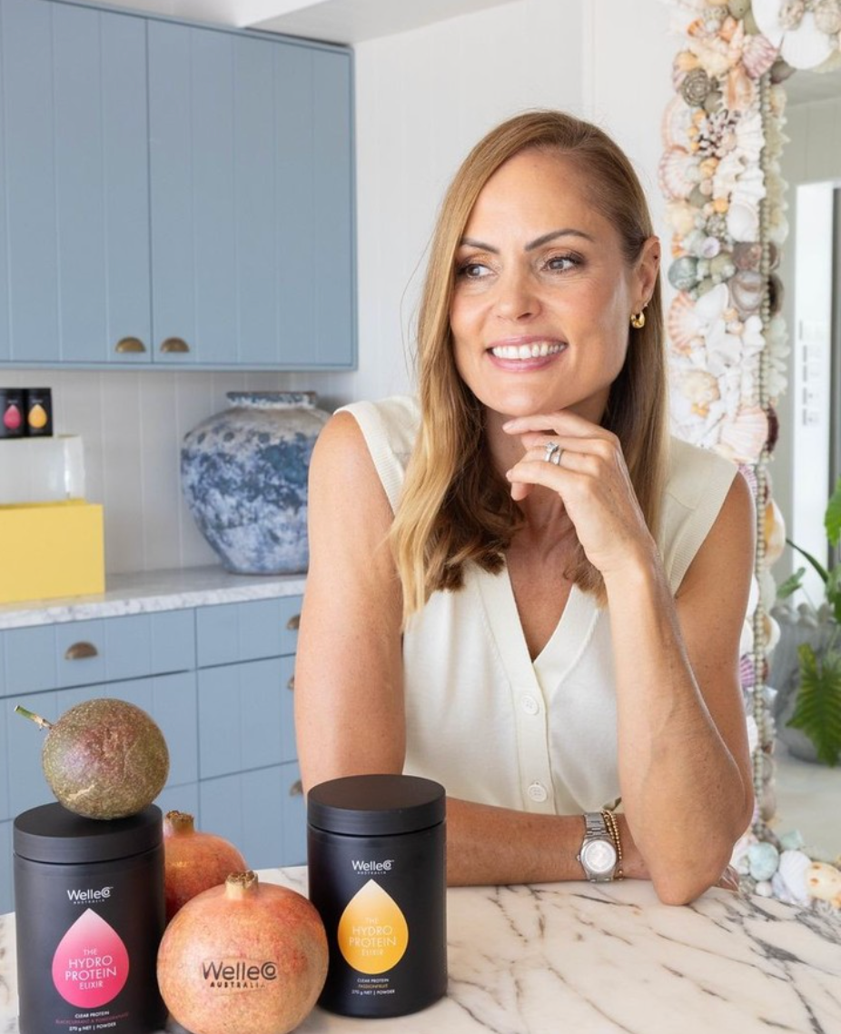 Woman smiling beside fruit and beauty products on a kitchen countertop.