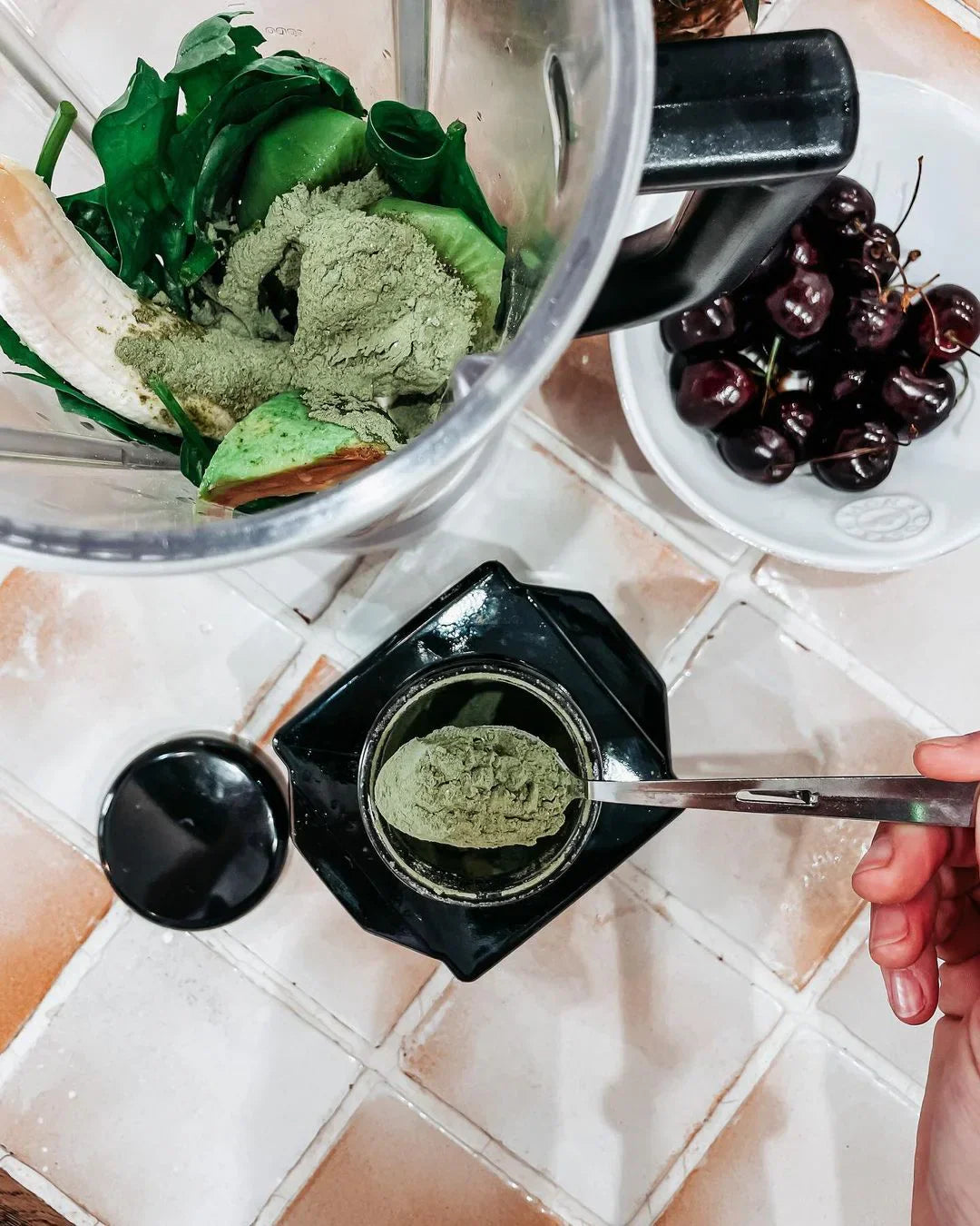 A blender with green ingredients and a bowl of cherries.